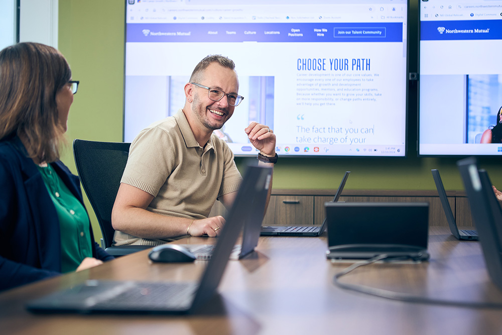 a person sitting at a table with laptops and a person in front of him